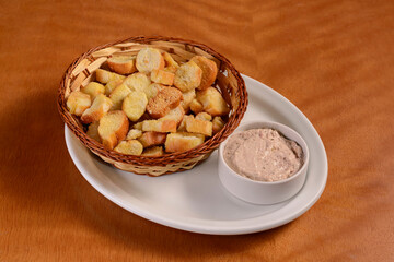 Portion of bite-size Brazilian toasted bread with pate on wooden table.
