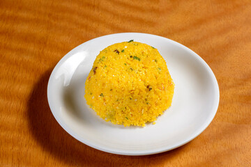 Couscous from the northeast region of Brazil on a white plate on a wooden table.