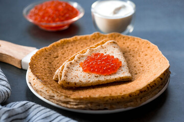 Russian traditions. Broad Maslenitsa. A stack of pancakes, sour cream and red caviar on a dark background. Close-up.