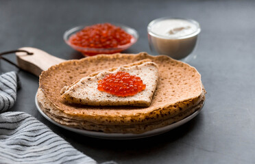 Russian traditions. Broad Maslenitsa. A stack of pancakes, sour cream and red caviar on a dark background. Close-up.