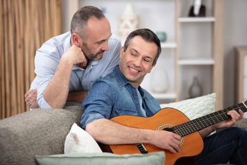 Fototapeta premium gay couple with guitar sitting on sofa at home