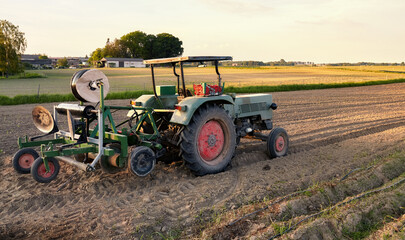 Tractor with plastic mulch layer on a field at sunset.