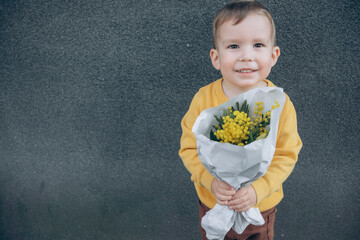 Cute little boy holding a bouquet of mimosa. Mimosa in children's hands
