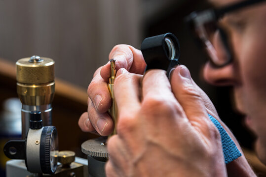 Jeweler faceting and evaluating under a pocket magnifier a small stone into brilliant cut attached on a metal dop