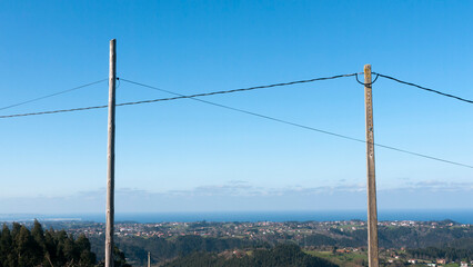 Cables entre poste de madera y hormigón sobre panorámica de casas y horizonte marino