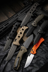 A variety of pocket military knives lie near the m4 carbine. Gray camouflage back.