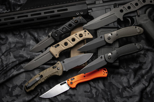 A variety of pocket military knives lie near the m4 carbine. Gray camouflage back.
