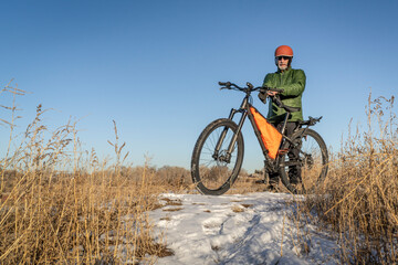 senior cyclist with a mountain bike on a trail covered by snow
