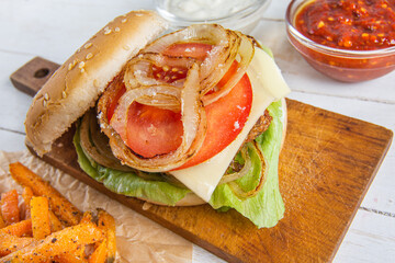 Detailed close up of healthy burger variant, caramelized onions, fresh tomatoes, lettuce, homemade garlic sauce and spicy chilli ketchup, stocky chicken steak and homemade sweet potatoes fries.