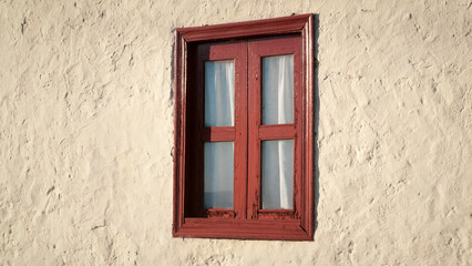 Ventana con marco de madera rojo y cortina en pared de estuco blanco de casa rural