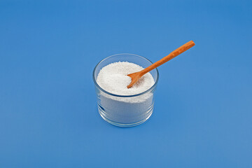 Sodium benzoate, sodium salt of benzoic acid in glass dish on blue background. White crystalline powder. Food additive E211 used as preservative in many foods, medicines, cosmetics