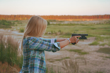A blonde girl aims a modern pistol at a shooting range.