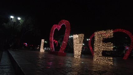 Letrero de amor iluminado con la palabra love escrita, con un corazón rojo iluminado con focos de baja intensidad en la calle 