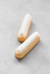 Two oval tartlets in the form of eclair with vanilla custard and delicate creamy jelly sprinkled with coconut chips on top. Light gray background