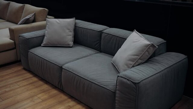 Gray sofa with two pillows filmed in a furniture store, in the background there is a comfortable brown sofa. 4k video.