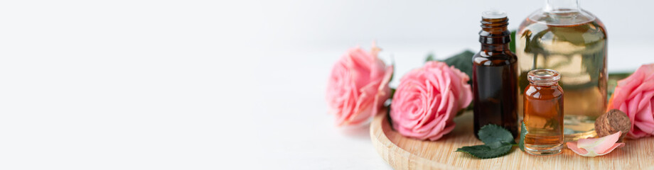 Aromatherapy. Pure organic essential rose oil concept. Elixir with plant based floral herbal ingredients. Pink flowers extract. Spa atmosphere with candle, towel. White background. Banner copy space