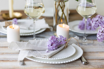 Fototapeta na wymiar Beautiful table decor for a wedding dinner with a spring blooming lilac flowers. Celebration of a special event. Fancy white plates, wineglasses, candles. Countryside style