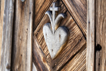 old wooden hart with cross pattern carved on wayside shrine door