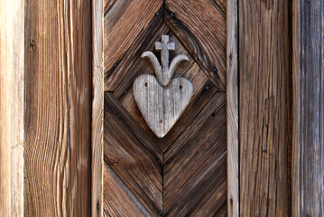 old wooden hart with cross pattern carved on wayside shrine door