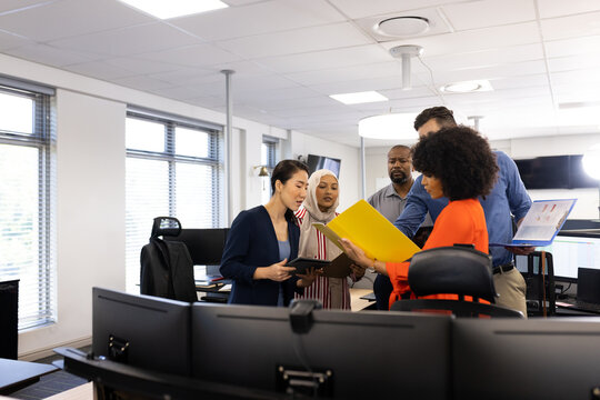 Happy diverse female and male businesspeople talking and working in office
