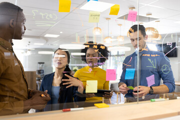 Diverse people in office brainstorming and writing on glass board