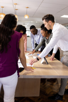 Vertical image of diverse female and male businesspeople talking and working