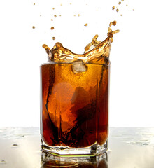 Glass of cola with splash and ice cubes on white.
