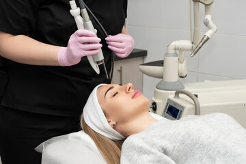 Doctor cosmetologist makes a laser dermal rejuvenation procedure to a patient. Against the background of a medical office with copy space.