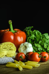 Ripe vegetables and uncooked pasta on wooden table on black background 