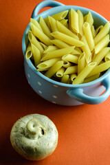 Top view of uncooked pasta in blue bowl and fresh mushroom on red surface