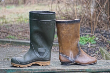 two rubber boots in green and brown are standing on a gray wooden table in the street