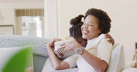 Smiling african american daughter giving happy mother a mother's day gift, slow motion