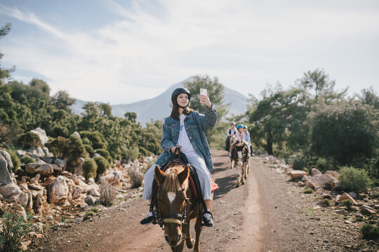 A young woman takes photos on her smartphone  riding a horse through picturesque landscapes.