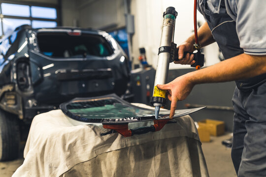 Worker applying an adhesive sealant to car windscreen preparing for replacement. High-quality 4k stock image.