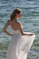 Fototapeta na wymiar Portrait of the bride in long white wedding dress with ocean water in the backgound