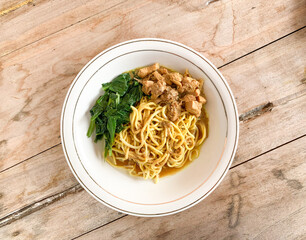 Noodle chicken soup (mie ayam) Indonesia food served on white bowl on wooden table.