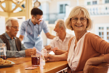 Happy senior woman playing cards with her friends at residential care home and looking at camera.