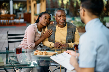 Black senior man and his daughter communicating with healthcare worker on patio at residential care home.