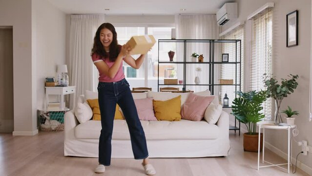 Asia people young Gen Z woman smile carry parcel box goods carton packaging happy joy fun dance at home. Omni channel enjoy buy gift order postal at retail online shop store fast courier send service.