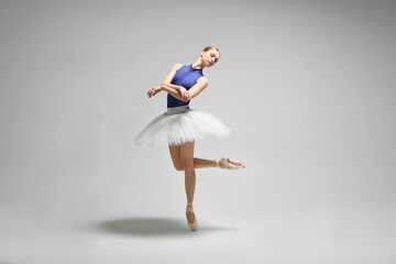 Fototapeta na wymiar Young ballerina practicing dance moves on light grey background