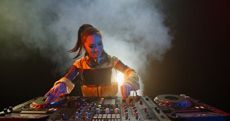 Cool female asian dj is working in a nightclub, standing at turntables, creating a dance music set...
