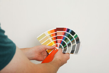 Man with palette choosing color for painting wall indoors, closeup. Interior design