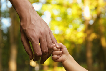 Daughter holding father's hand outdoors, closeup. Happy family