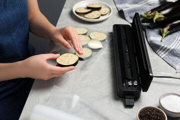 Woman packing cut eggplant into plastic bag using vacuum sealer on light grey marble table, closeup