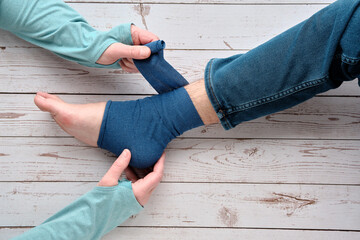 An adult wrapping compression bandage around sprained ankle of teenage boy to reduce ache. Feet...