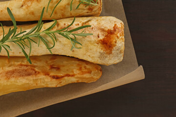 Tasty baked parsnips and rosemary on wooden table, top view