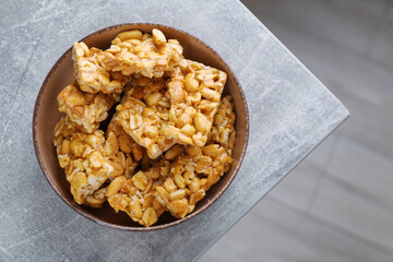 Bowl with delicious peanut kozinaki bars on light gray textured table, top view. Space for text