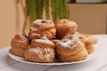 Delicious profiteroles with powdered sugar on white wooden table