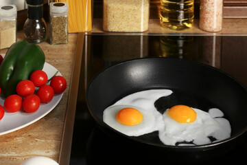 Cooking eggs for breakfast in frying pan on cooktop