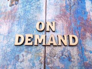 Wooden word on a blue wooden background with the word ON DEMAND